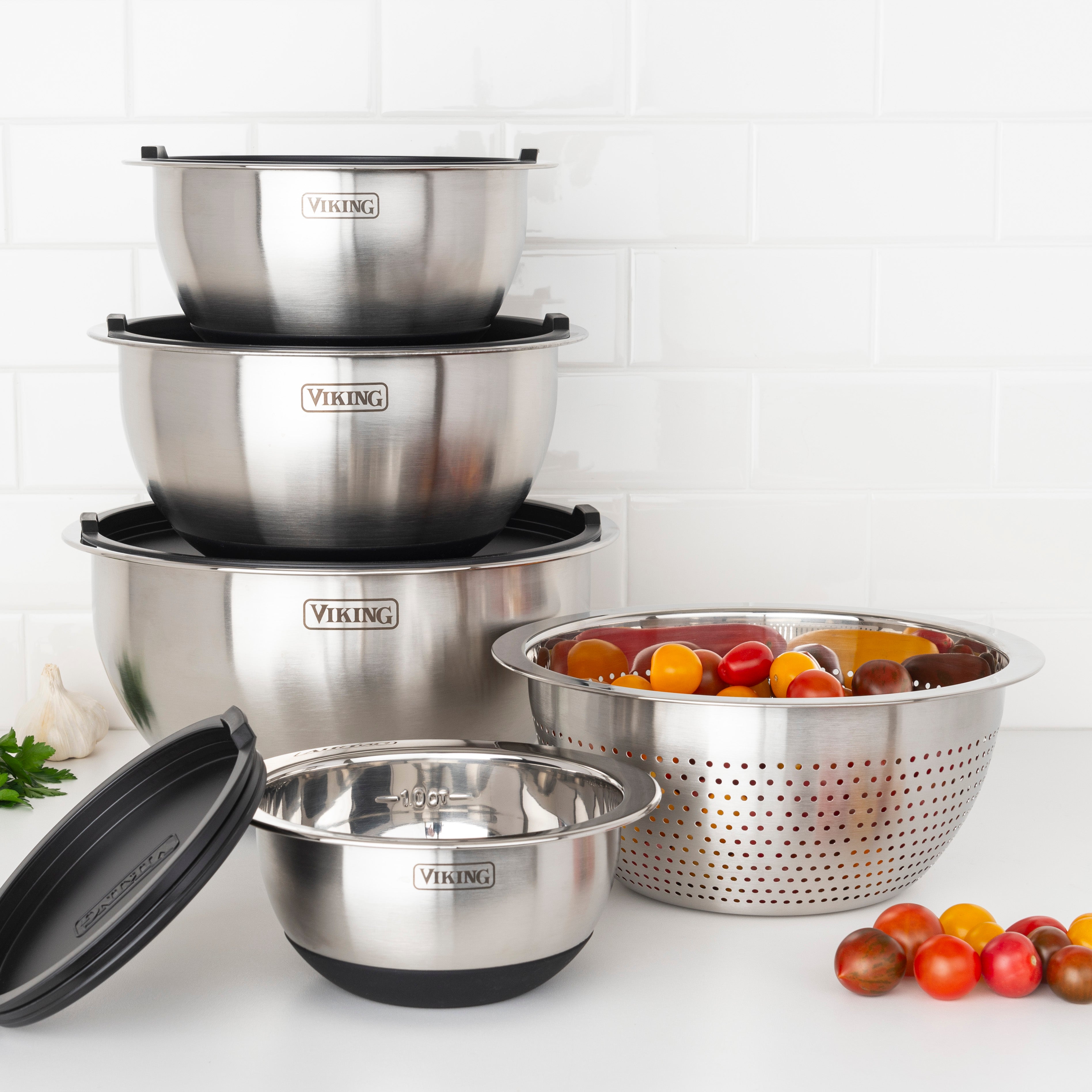 The Viking 9-Piece Stainless Steel Mixing Bowl Set with Strainer by Viking Culinary Products includes four bowls with silicone bases, three airtight lids, and a matching colander, displayed against a white tiled kitchen backsplash.