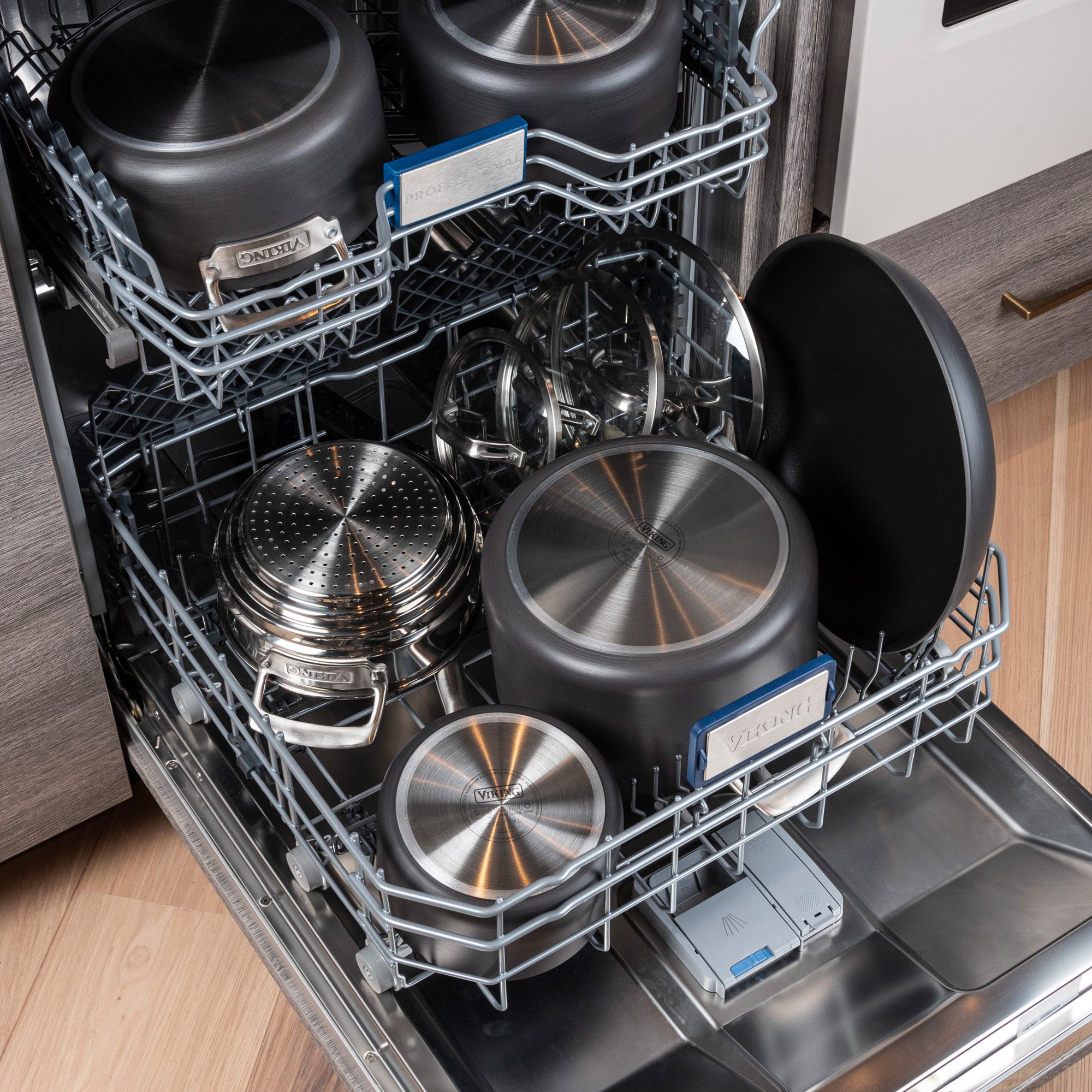 An open dishwasher displays a Viking Hard Anodized Nonstick 15-Piece Cookware Set with glass lids by Viking Culinary Products, neatly arranged on racks in a modern kitchen with wood flooring.