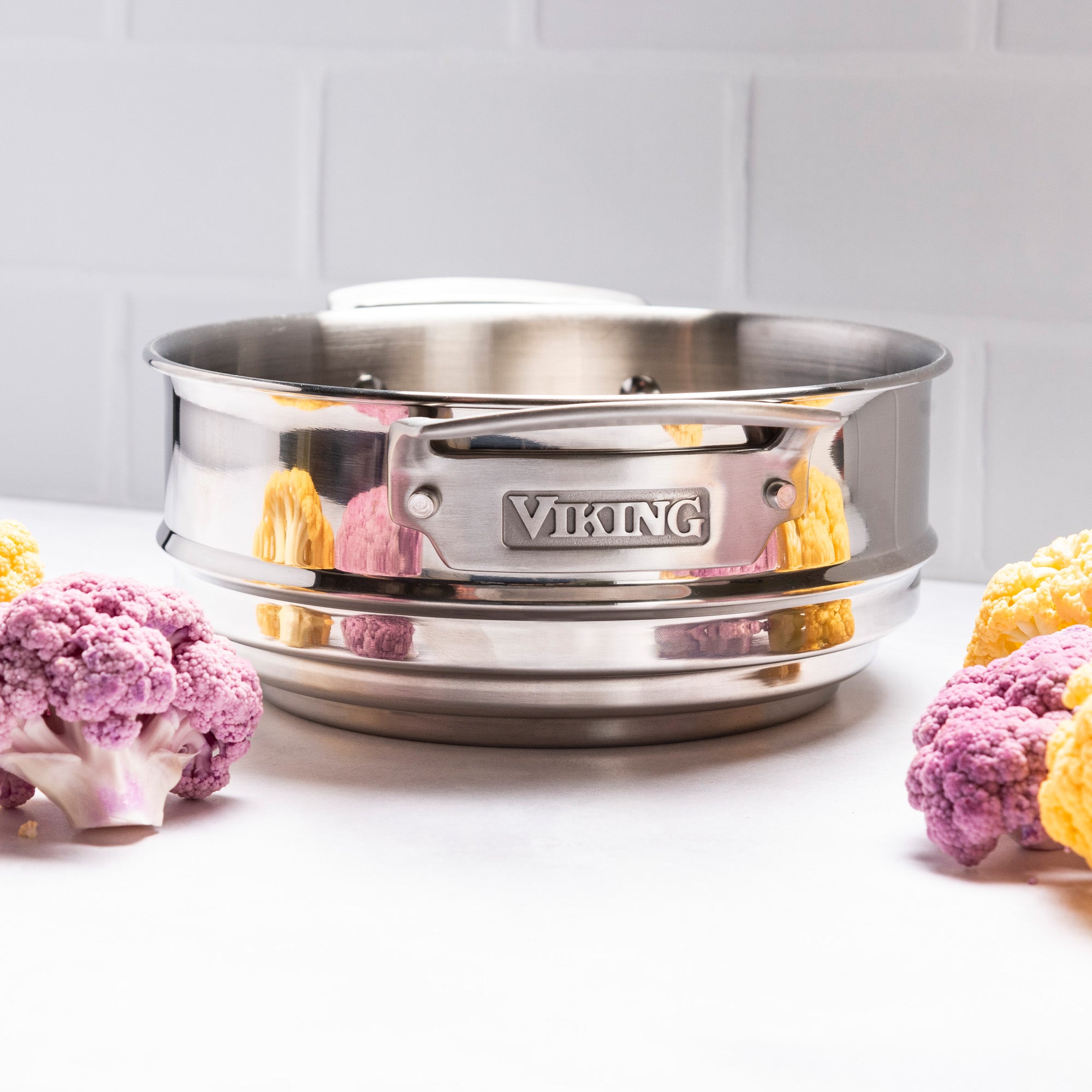 A Viking Culinary Products Hard Anodized Ceramic Nonstick pot from the 12pc Cookware Set sits on a white surface with purple and yellow cauliflower florets, set against a backdrop of white tiles.