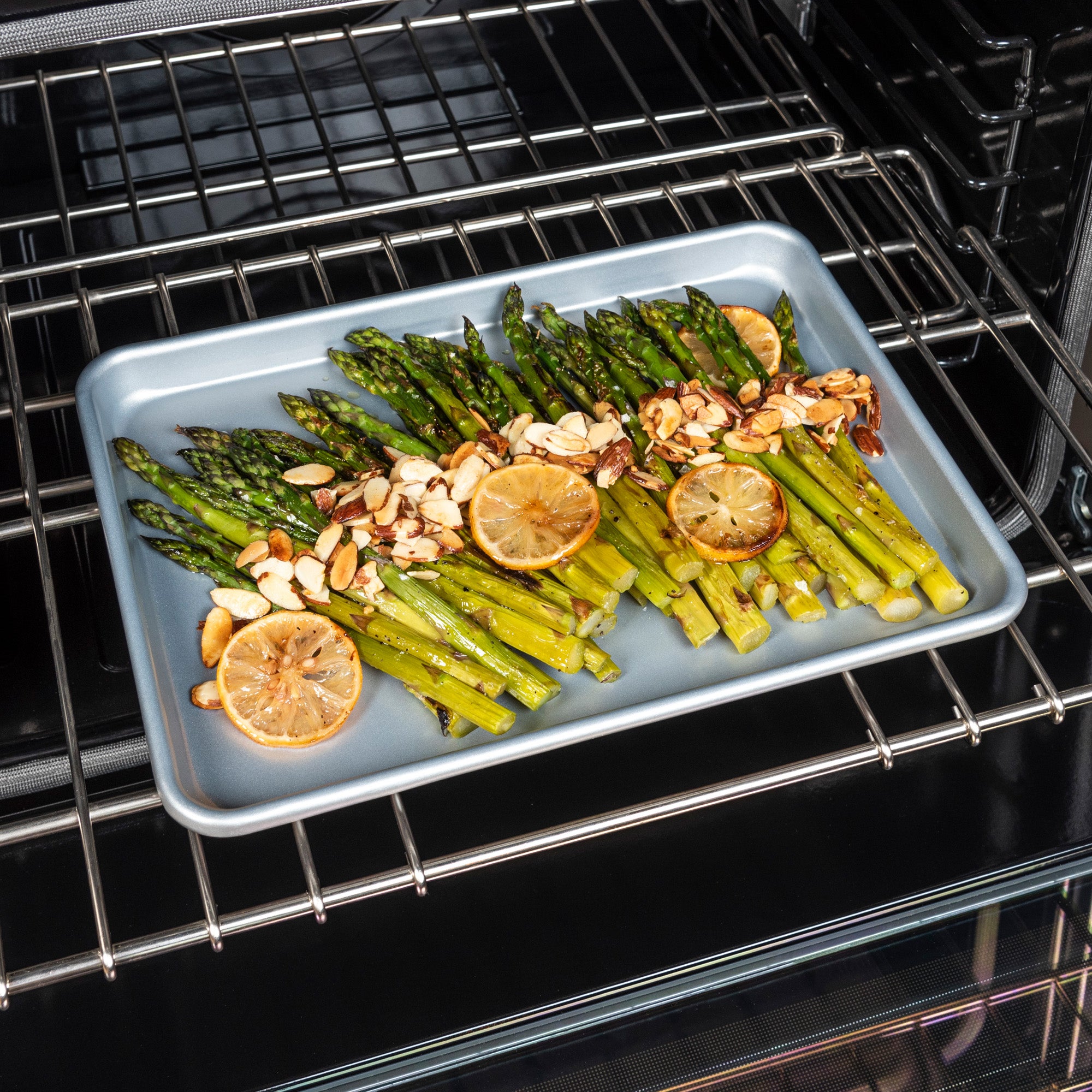 The Viking Culinary Products 13-Inch Aluminized Nonstick Baking Sheet holds roasted asparagus, lemon slices, and almonds. Its heavy-duty aluminized steel ensures even heating and the nonstick coating allows for easy cleanup.