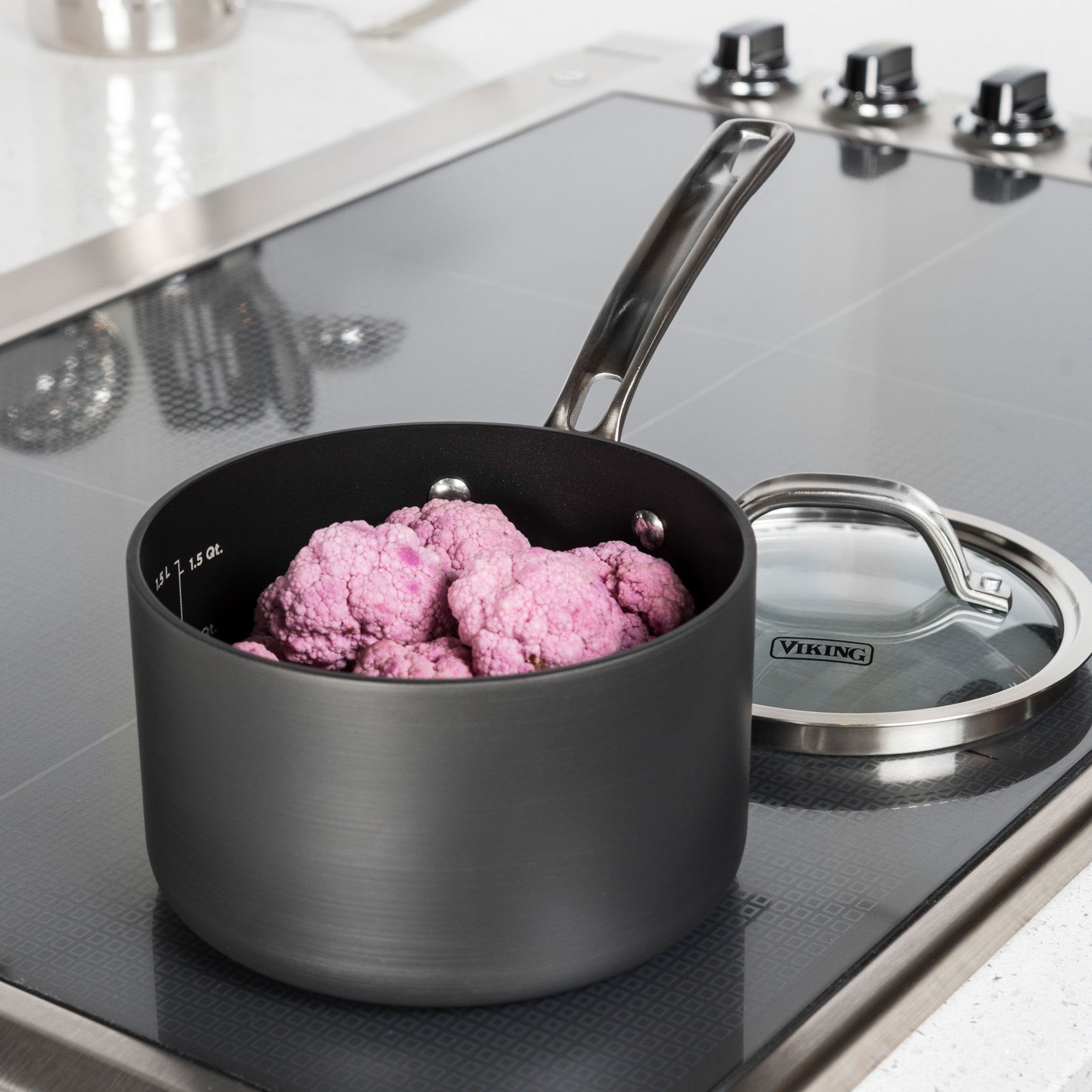 A Viking Hard Anodized Nonstick 2-Quart Sauce Pan by Viking Culinary Products sits on the stove with raw purple cauliflower inside. Its glass lid is nearby, and the pan features a stay-cool handle.