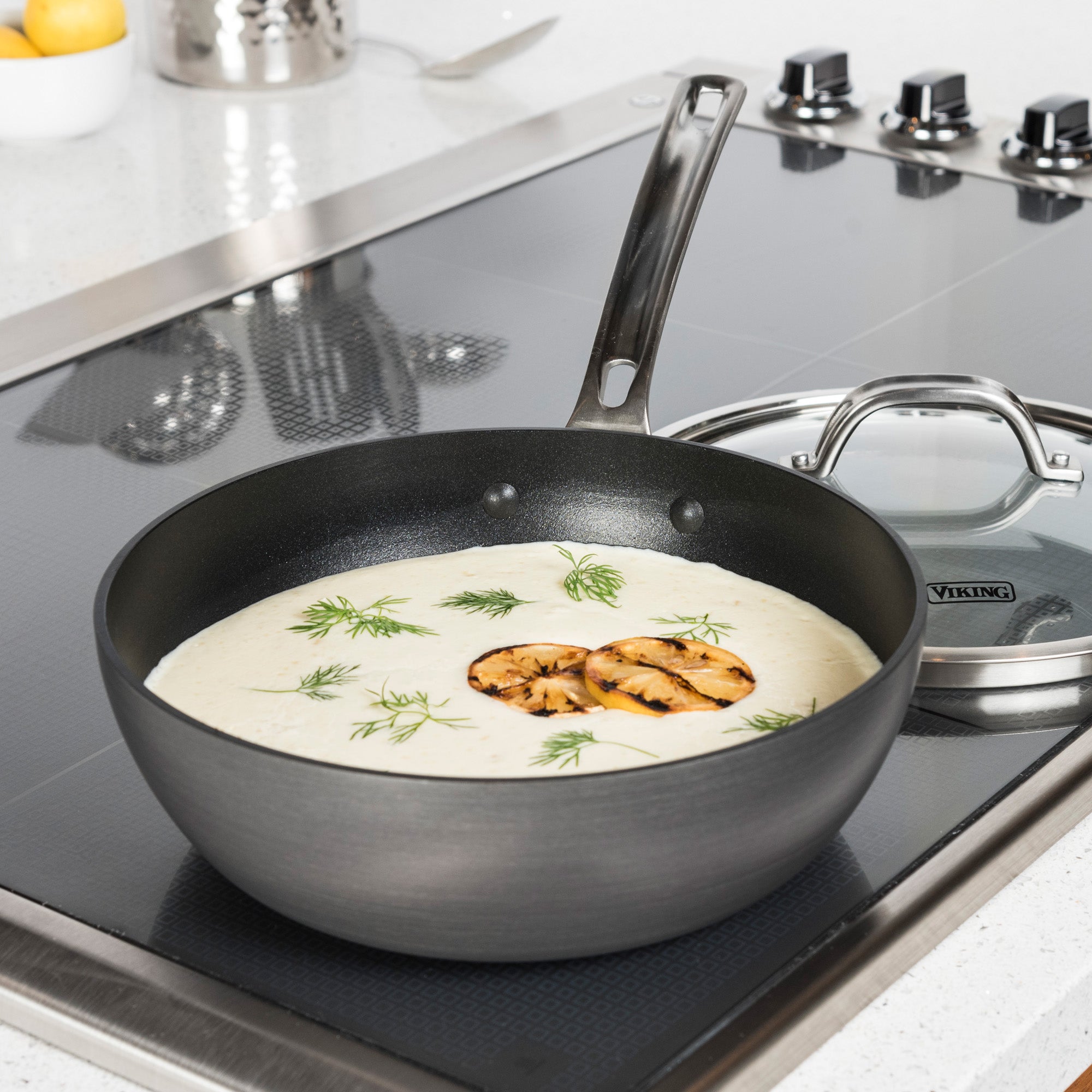 A Viking Hard Anodized Nonstick 3-Quart Saucier Pan by Viking Culinary Products sits on the stove with creamy white sauce, grilled mushrooms, and dill. Its glass lid with Viking Stay-Cool Handles rests nearby.
