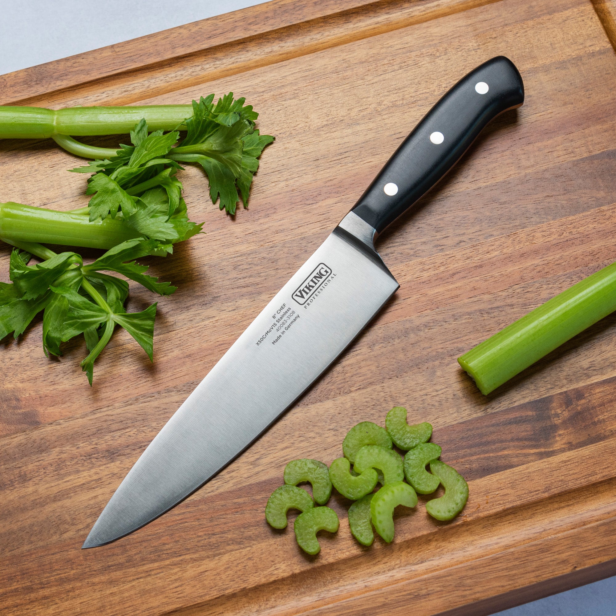 The Viking Culinary Products Viking Professional 8-Inch Chefs Knife with a full-tang design rests on a wooden cutting board, surrounded by celery stalks, leaves, and several sliced celery pieces.