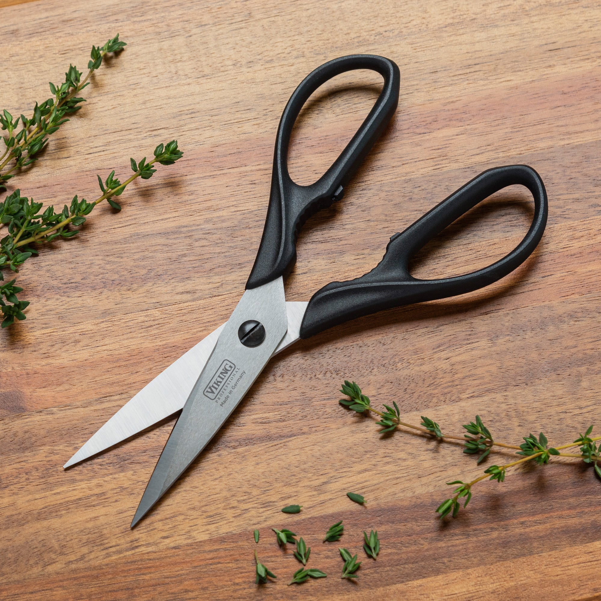 A pair of Viking Professional 8-Inch Scissors by Viking Culinary Products, featuring dishwasher-safe black handles, rests on a wooden surface next to a few sprigs of fresh thyme.