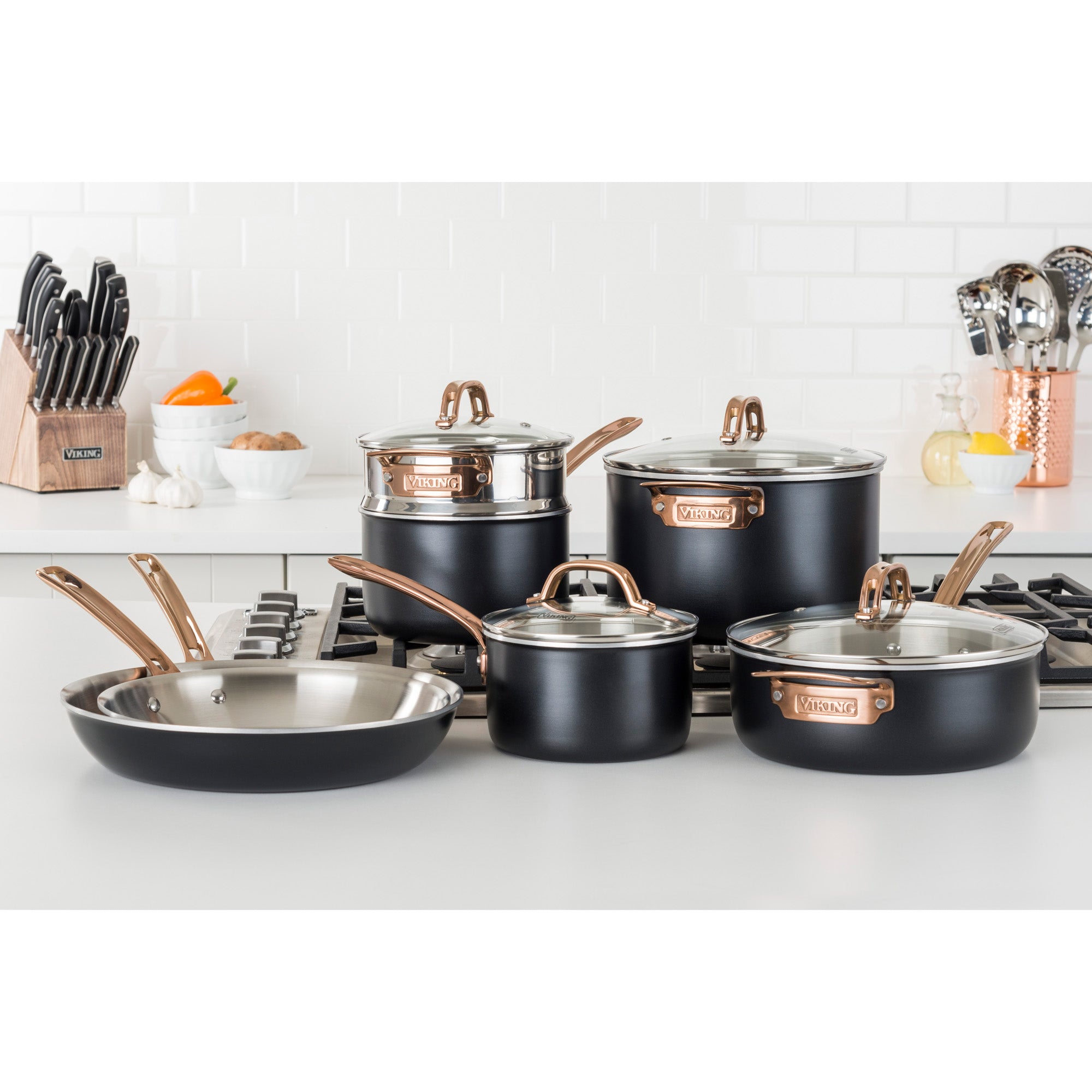The Viking Culinary Products 3-Ply 11 Piece Black and Copper Cookware Set with Glass Lids is displayed on a white kitchen counter alongside a knife block, utensils, eggs, and various kitchen items.