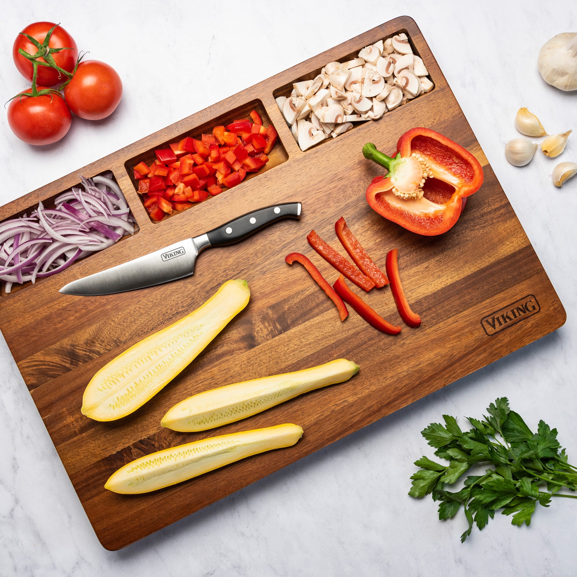 The Viking Acacia 20-Inch Reversible Butcher Block Prep and Carving Board by Viking Culinary Products holds sliced mushrooms, diced red bell pepper, sliced red onion, plus a chefs knife, zucchini, chili peppers, tomatoes, garlic, parsley, and half a bell pepper.