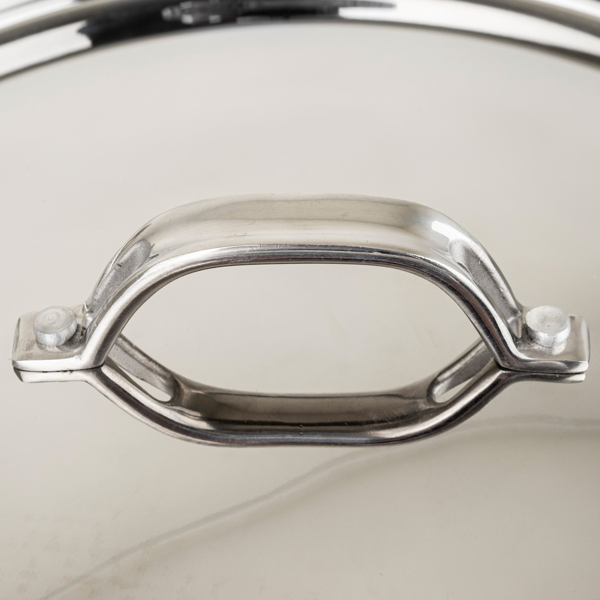 Close-up of the Viking Culinary Products Contemporary 4-Ply Copper Clad 9-Piece Cookware Sets metal lid handle. Its stay-cool, shiny stainless steel design ensures safety, while the glass beneath underscores this quality cookware set.