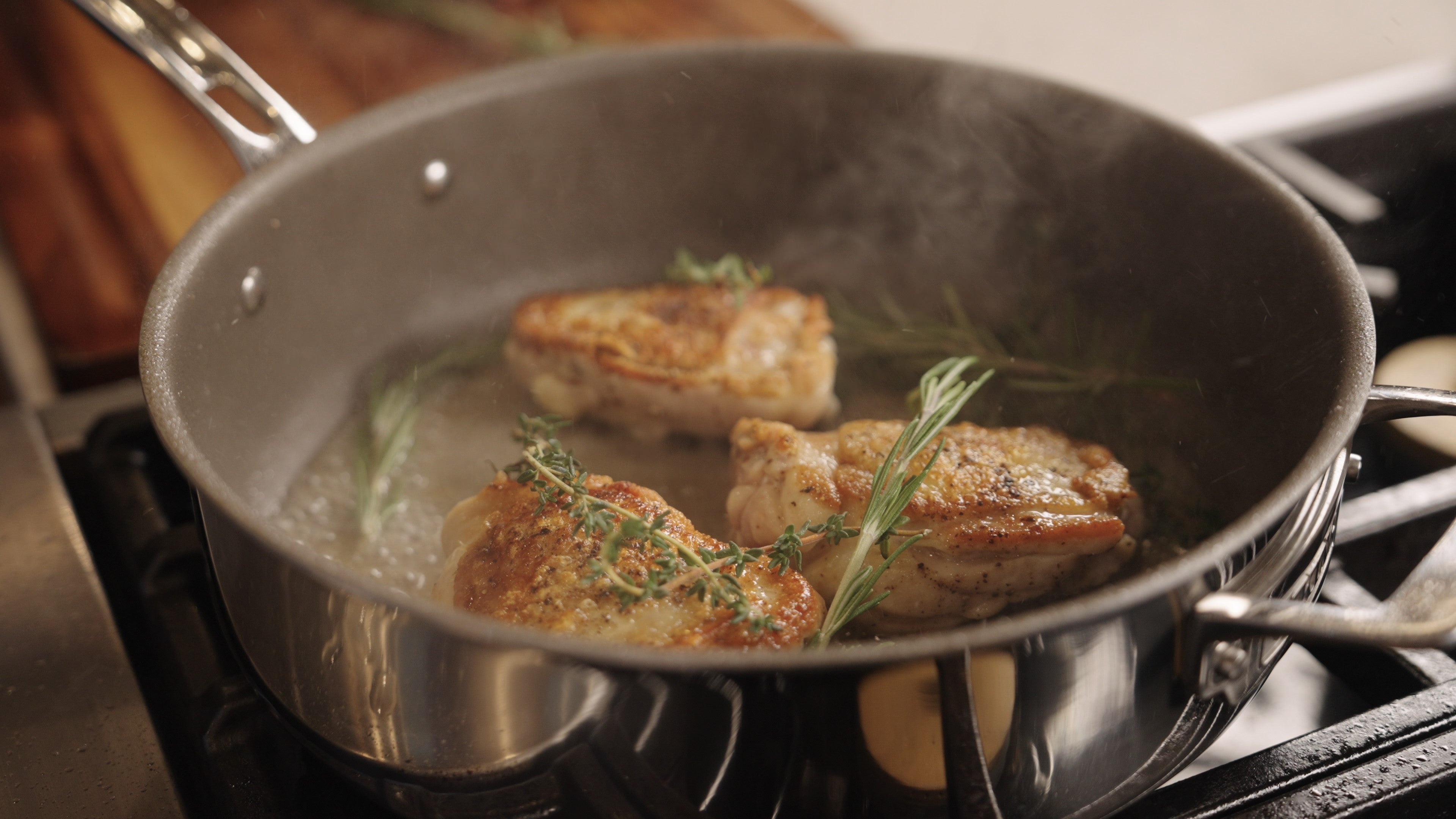 Close-up of a stainless steel pan on a stove, cooking a colorful dish with vegetables and pieces of meat. The word Viking is engraved on the pans handle. Steam rises from the hot food.