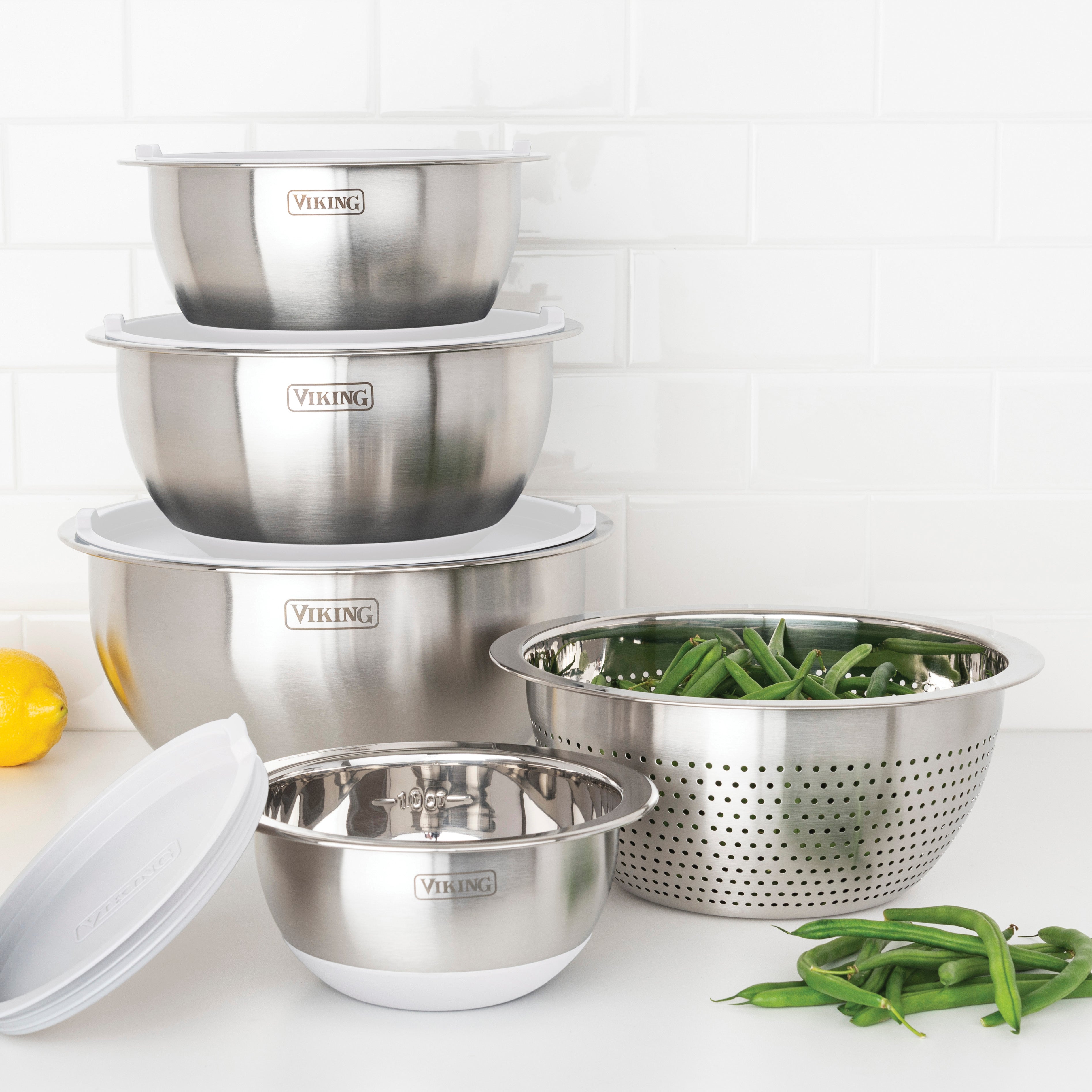 The Viking 9-Piece Stainless Steel Mixing Bowl Set with Strainer by Viking Culinary Products sits on a kitchen counter near green beans, the frost white lids keeping ingredients fresh against a backdrop of white subway tile.