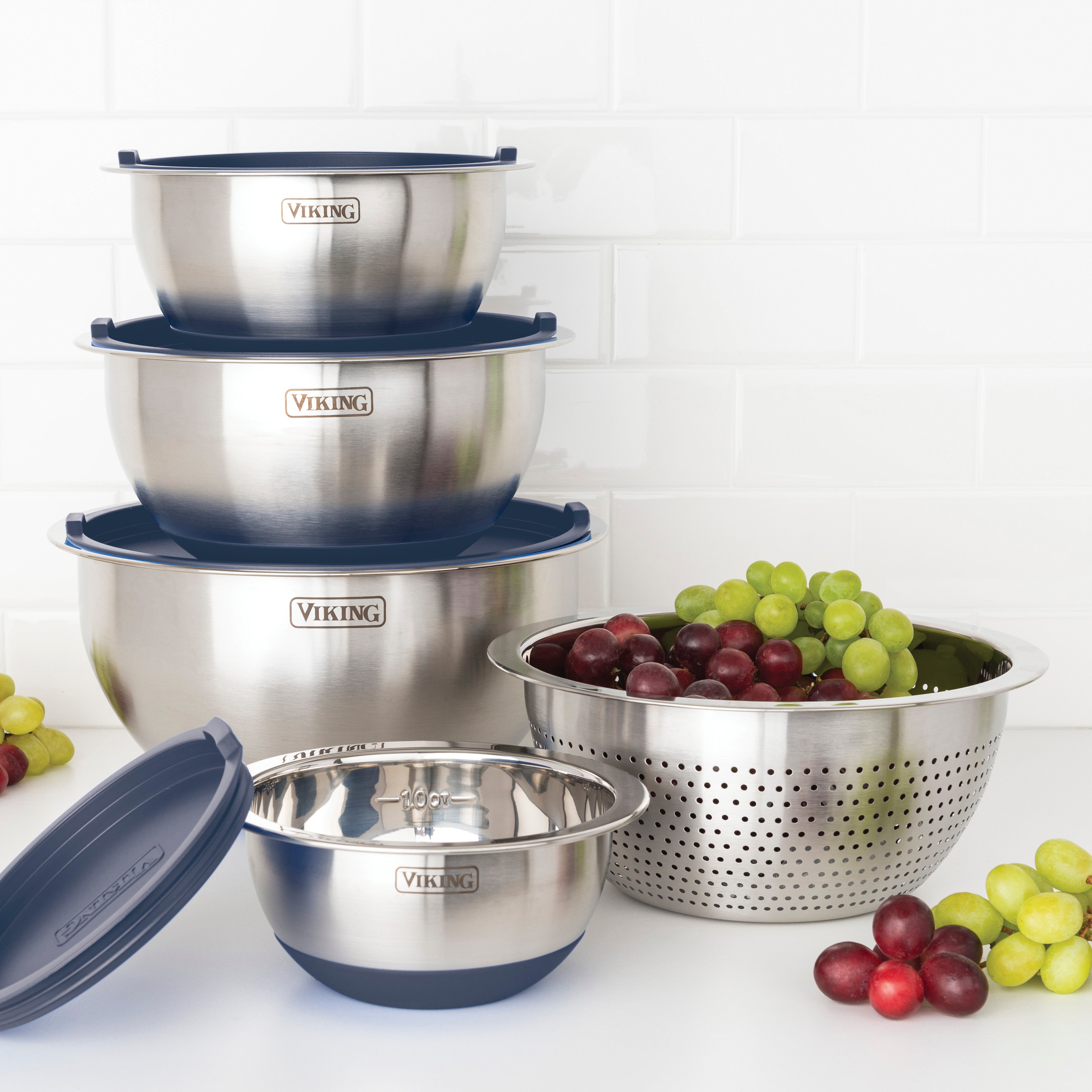 The Viking Culinary Products 9-Piece Stainless Steel Mixing Bowl Set with Strainer in Slate Blue is stacked next to its colander filled with green and red grapes, with extra grapes on a white countertop against a white tile wall.