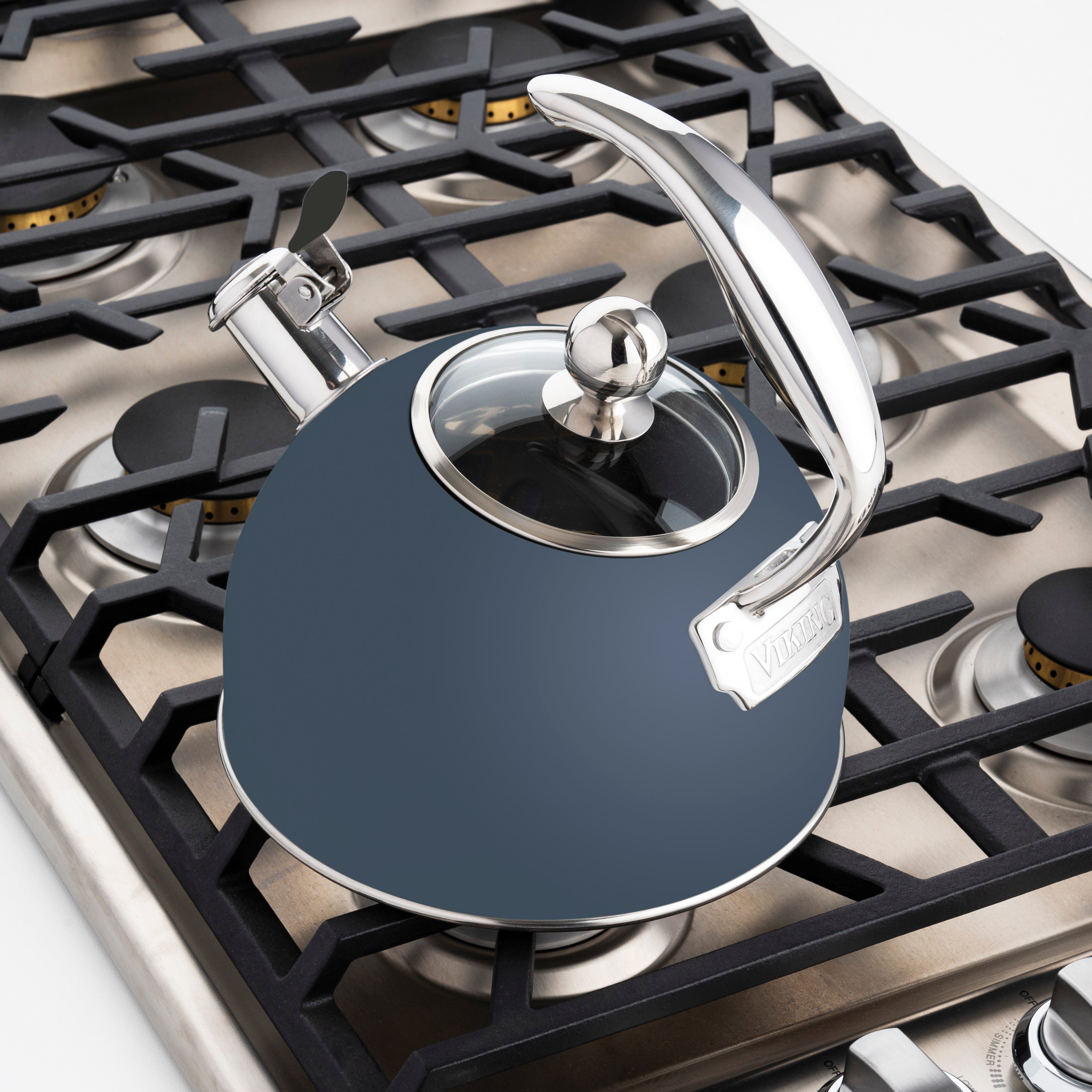 A Viking Culinary Products 2.6-quart slate blue stainless steel whistling kettle with a 3-ply base sits on a stainless steel gas stove, with black grates and burner controls visible.