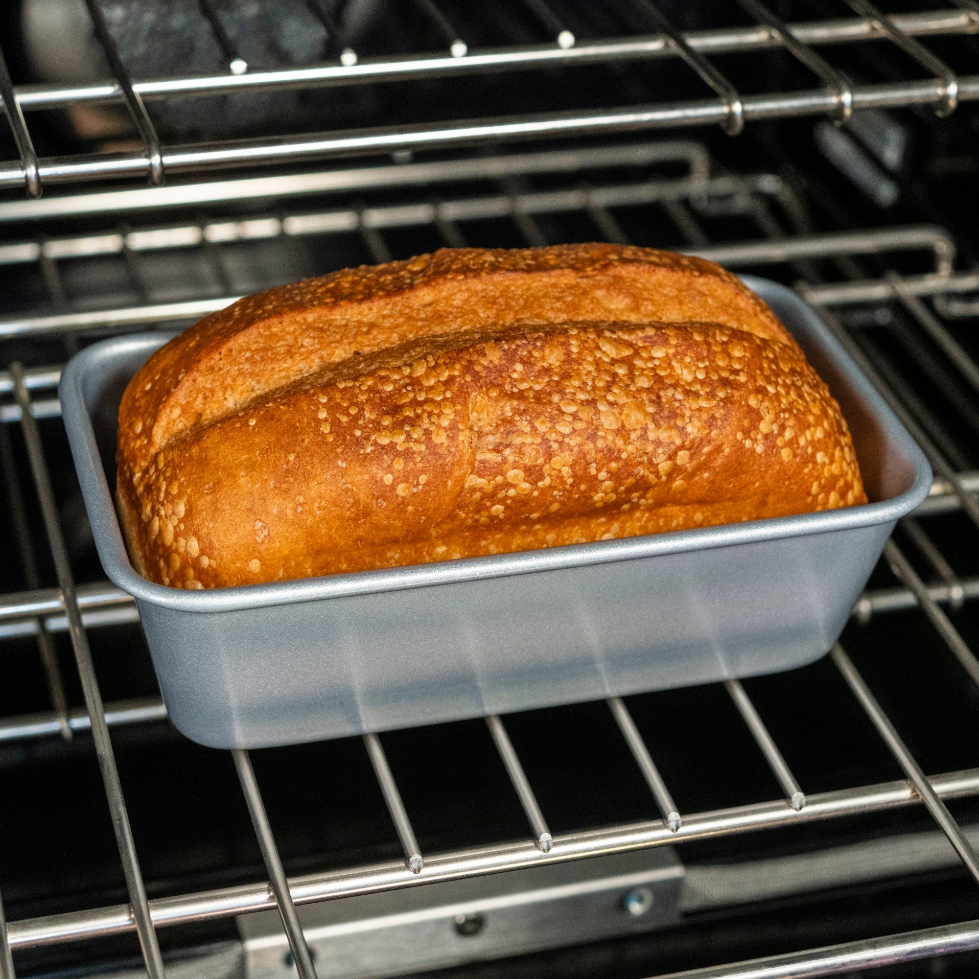 A golden-brown loaf rests in the Viking Aluminized Steel Nonstick 9-inch Loaf Pan by Viking Culinary Products, fresh from the oven with a crisp crust and textured surface.