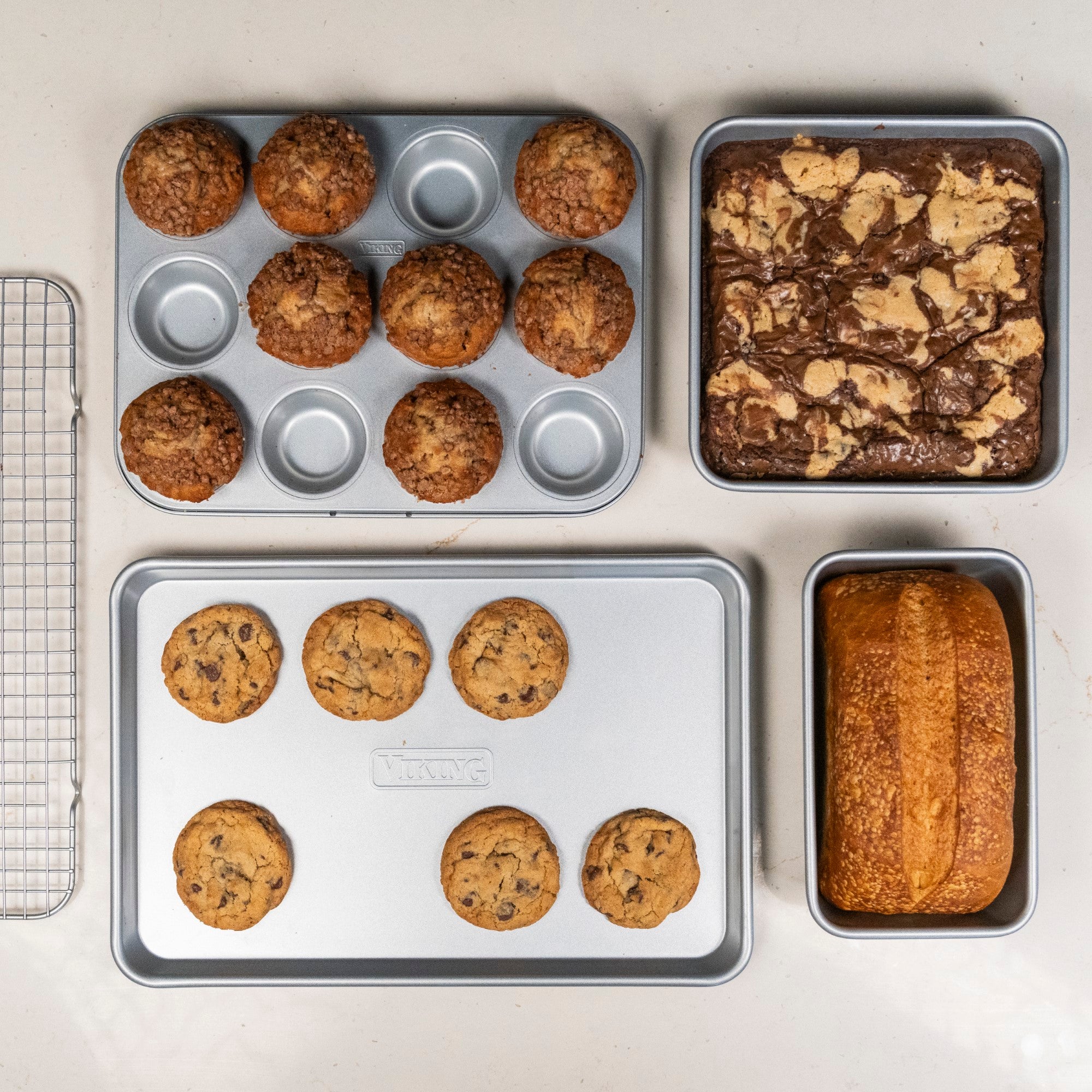 A top-down view shows the Viking Aluminized Steel Nonstick 5-pc Bakeware Set by Viking Culinary Products with muffins, marbled brownies, chocolate chip cookies, and a loaf of bread on various pans and racks.
