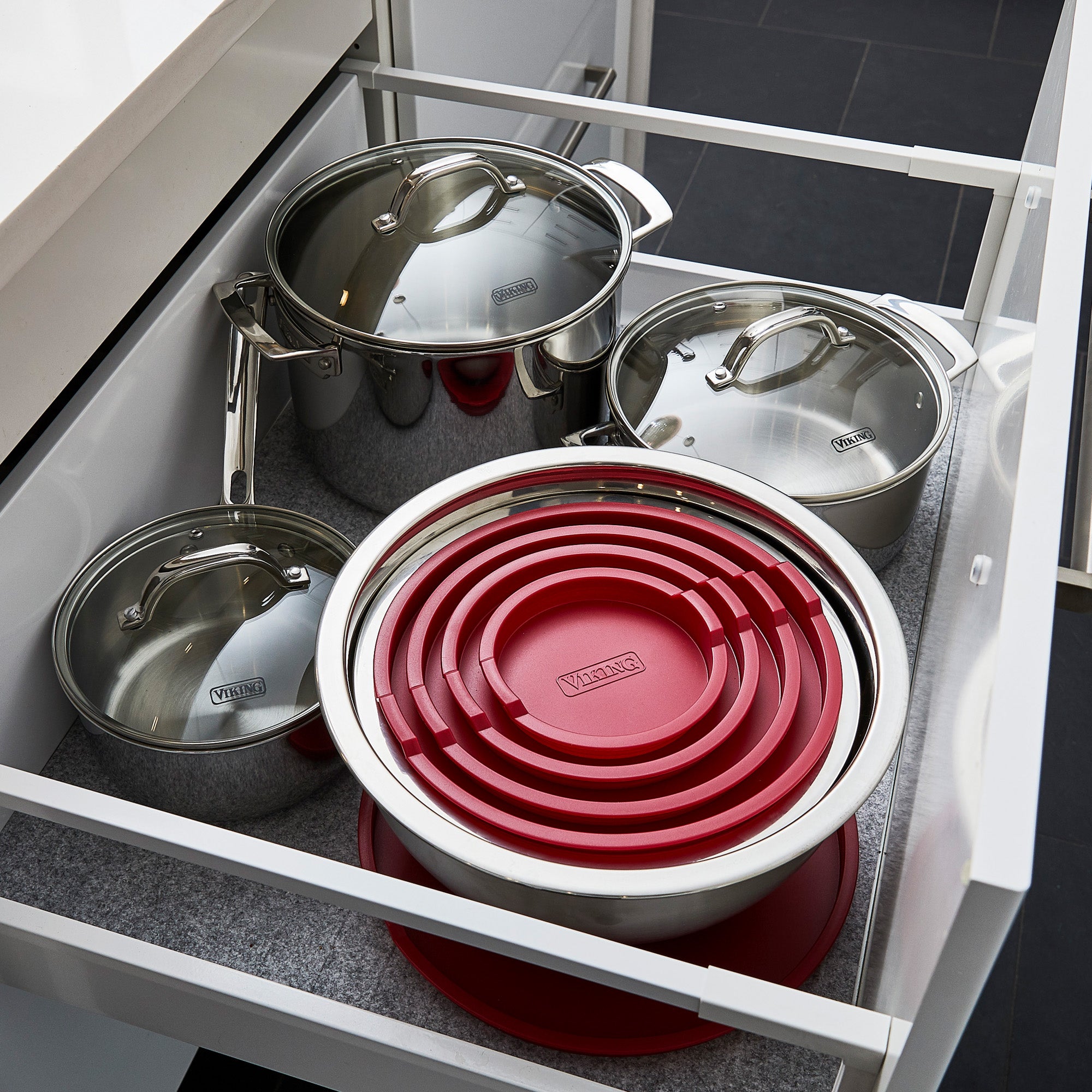 A kitchen drawer holds the Viking Culinary Products 10-Piece Stainless Steel Mixing Bowl Set with red lids, stacked neatly for compact storage.