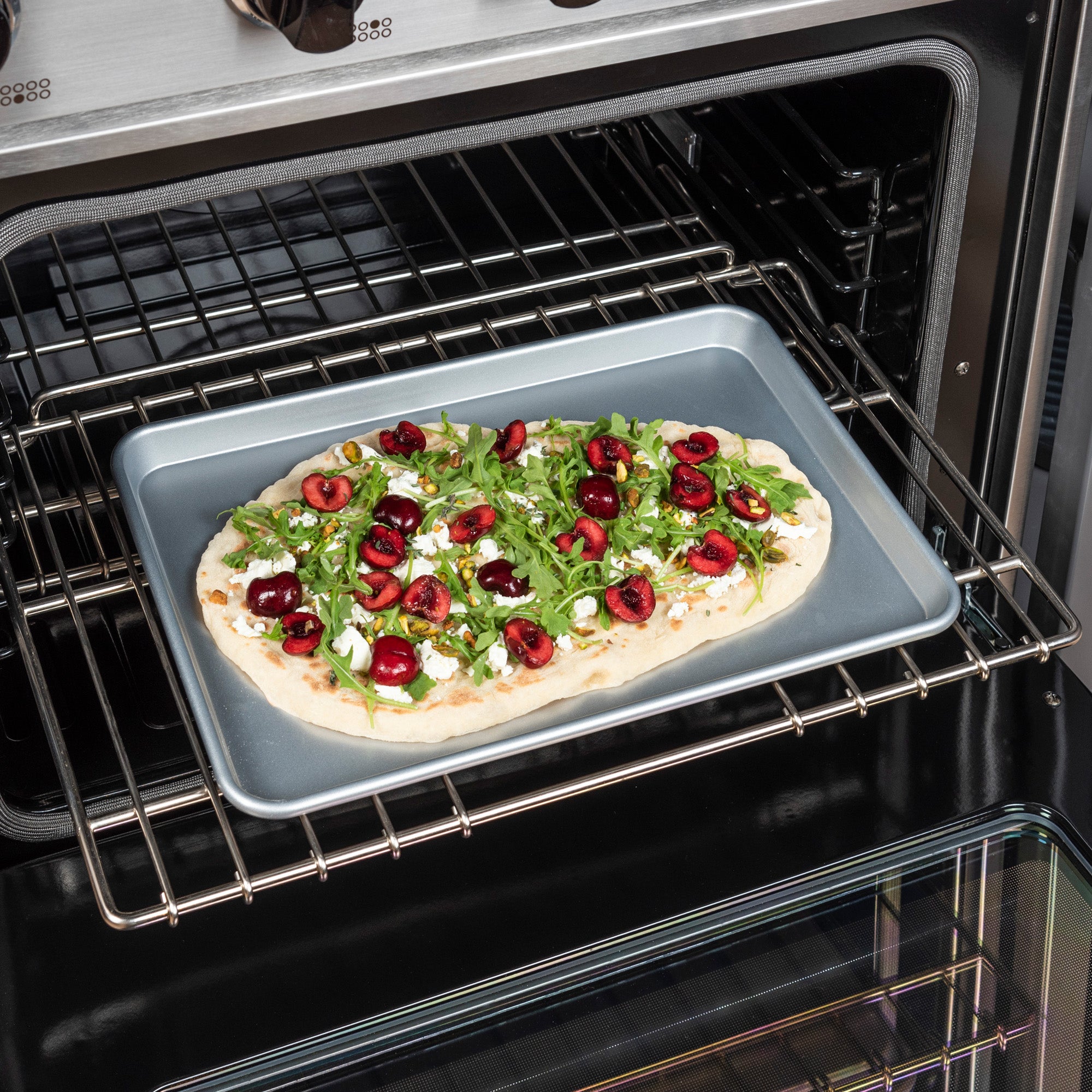 A flatbread with arugula, cherries, and cheese is baking on the Viking 3-Piece Nonstick Aluminized Steel Baking Sheet Set by Viking Culinary Products, ensuring easy release and pro results with every use.