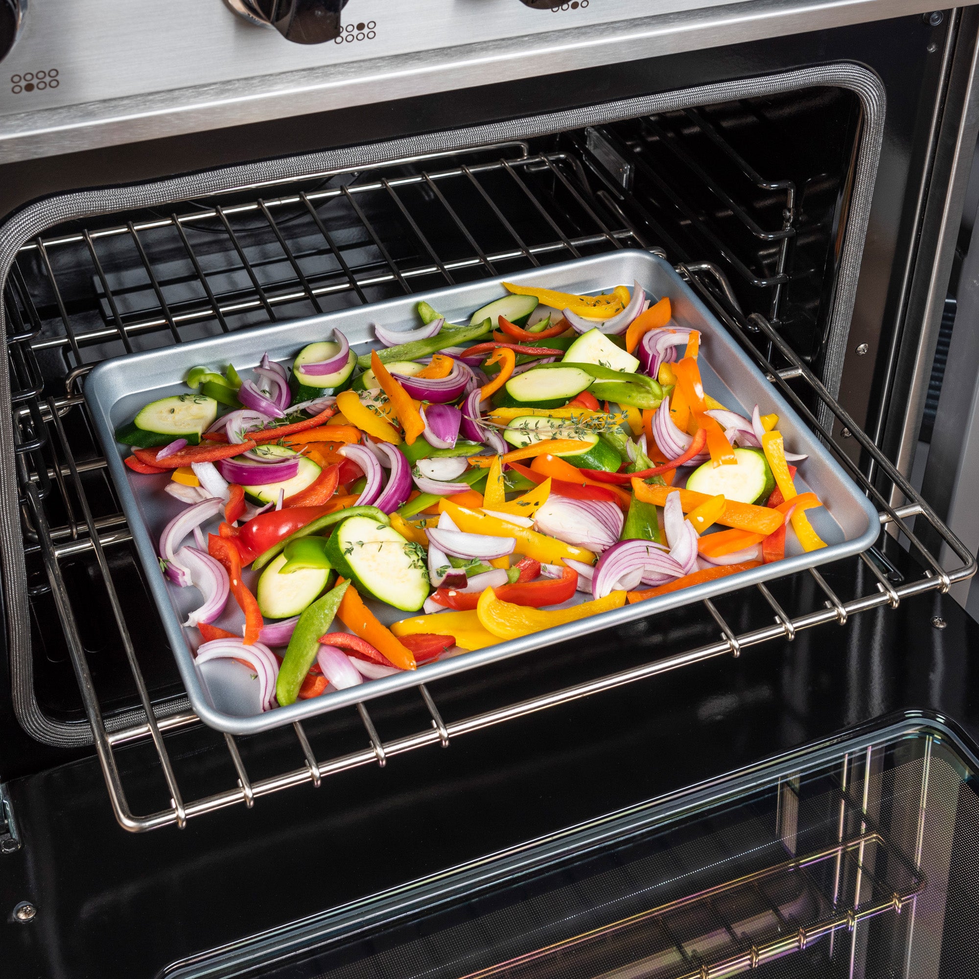 A Viking 3-Piece Nonstick Aluminized Steel Baking Sheet from Viking Culinary Products holds sliced zucchini, red onion, and bell peppers in an open oven, ready to roast for professional baking results.