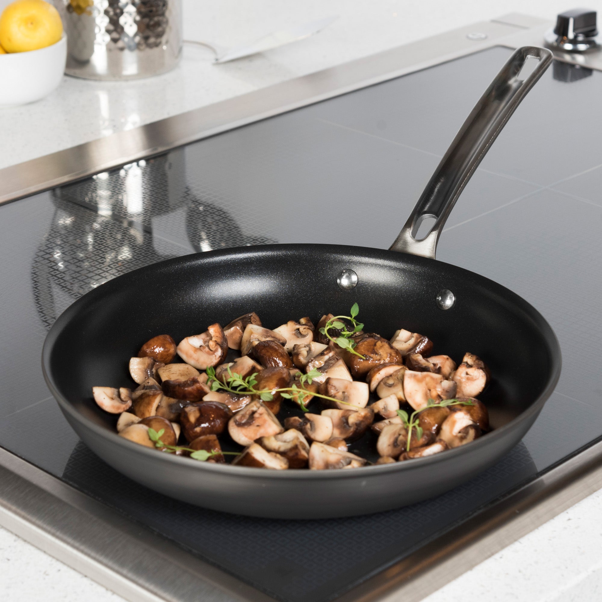 The Viking Hard Anodized Nonstick 2-Piece Fry Pan Set by Viking Culinary Products sizzles with chopped mushrooms and fresh herbs on a stovetop in a modern kitchen, featuring signature Stay-Cool Handles.