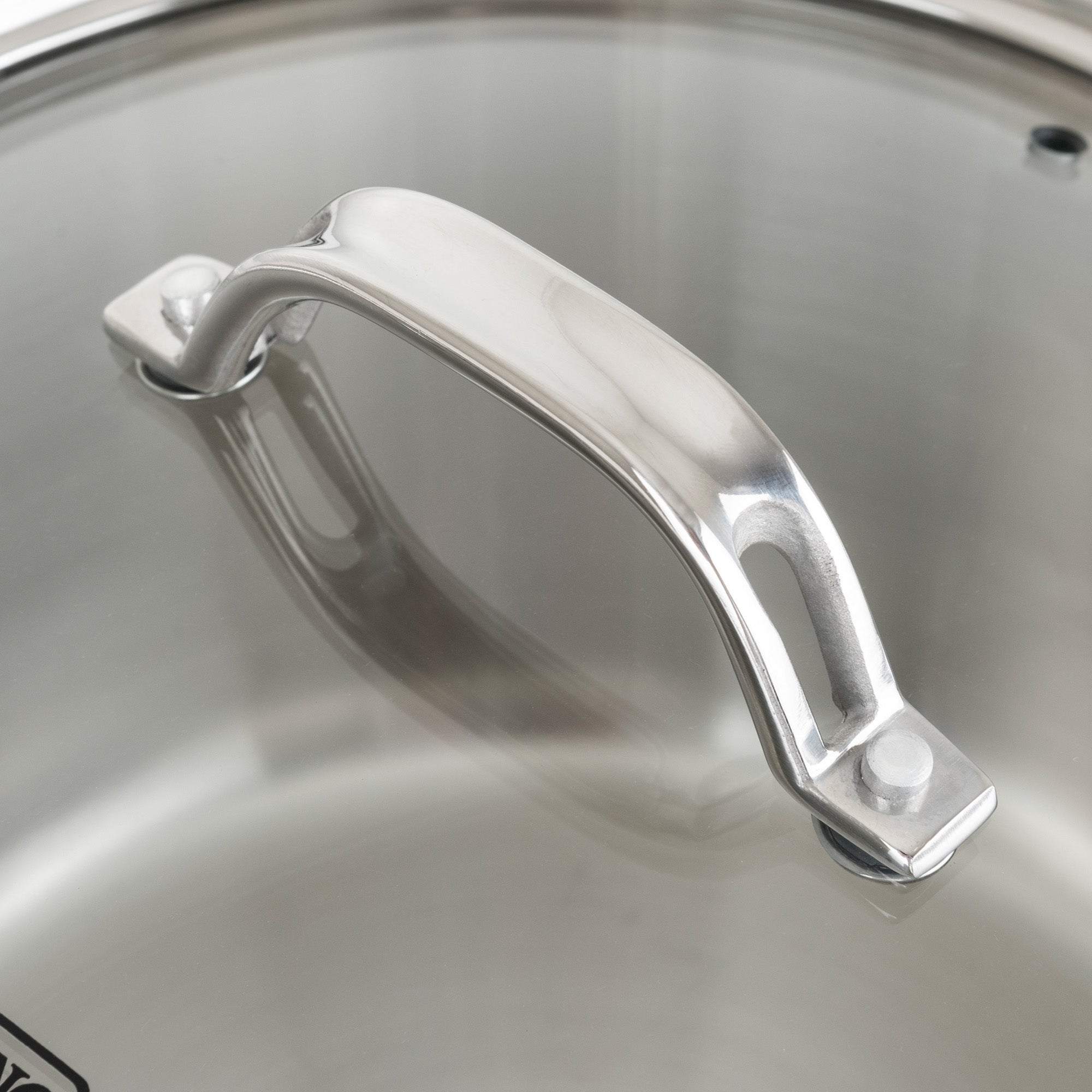 Close-up of a shiny stainless steel handle on a glass lid, showcasing smooth curves and secure rivetsâ€”an elegant feature of the Viking Contemporary 3-Ply Stainless Steel 10-Piece Cookware Set by Viking Culinary Products.