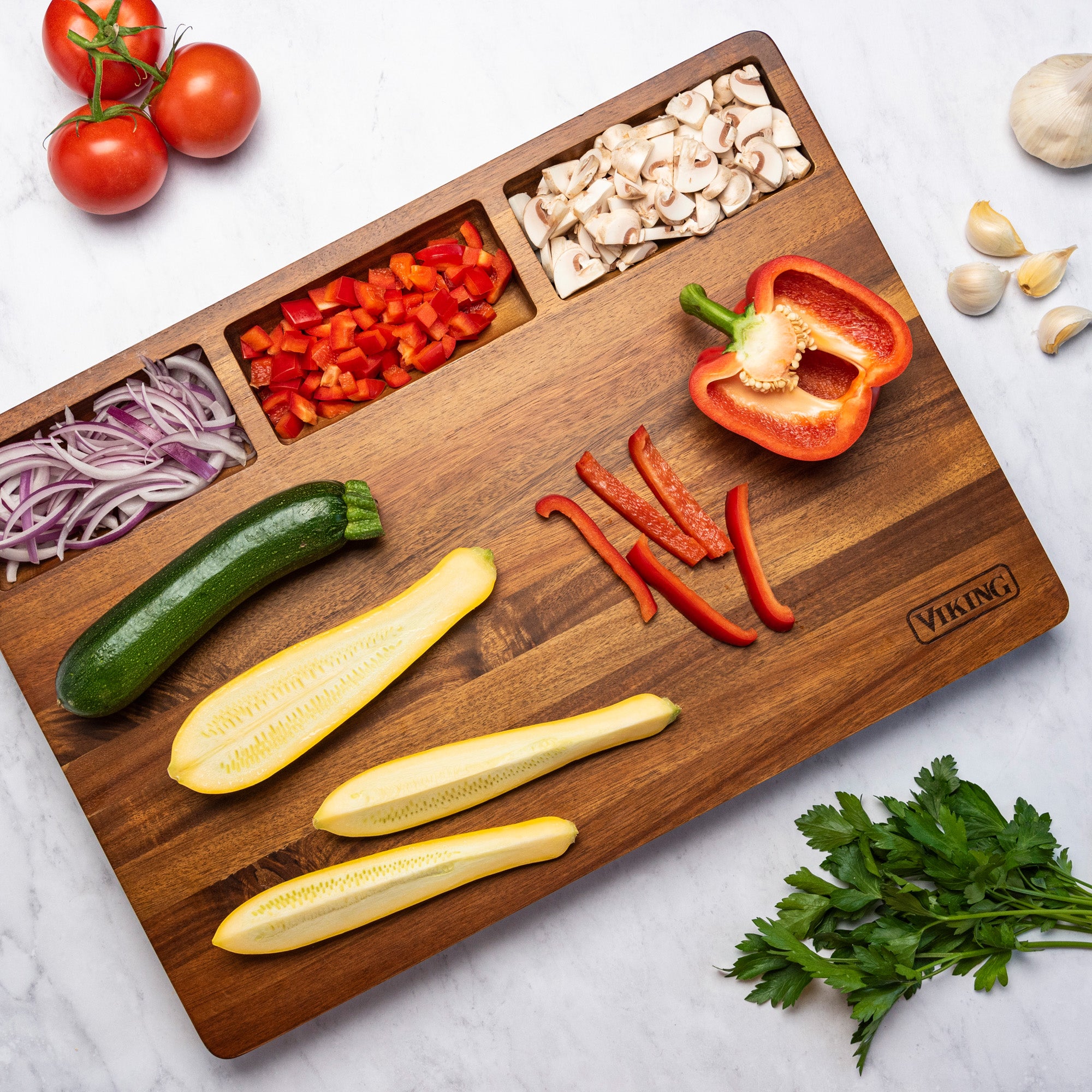 The Viking Acacia 20-Inch Reversible Butcher Block Prep and Carving Board by Viking Culinary Products displays chopped red bell pepper, mushrooms, red onion, halved zucchini, yellow squash, and sliced red pepper with whole veggies nearby.
